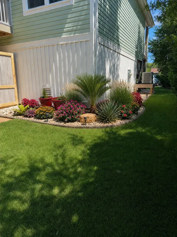 Corner flower bed with a palm, blooming shrubs and a river rock border beside a fresh-cut lawn